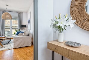 A modern living room with a sofa, a wooden side table with a vase of flowers, and a large mirror on the wall. - Solaga - Christina (Málaga)