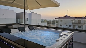 A rooftop hot tub with a glass enclosure, a large umbrella, and a city view at sunset. - STAY Oasis Luxury Villa 5 (Ayia Napa)