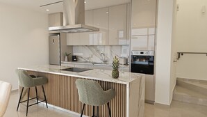 A modern kitchen with a marble countertop, two bar stools, a stainless steel range hood, a built-in oven, and a wooden panel backsplash. - STAY Oasis Luxury Villa 5 (Ayia Napa)
