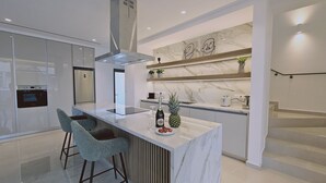 Et moderne køkken med marmorbordplade, rustfrie stålapparater og en bar med barstole.