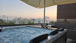 En tagterrasse med jacuzzi, udendørs møbler og udsigt til bygninger i det fjerne.