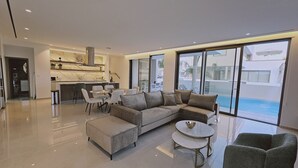 En moderne stue med en hjørnesofa, et spisebord og udsigt til en swimmingpool.