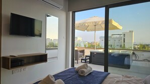 Ein modernes Hotelzimmer mit einem großen Bett, einem Flachbildfernseher, einem Balkon mit Sonnenschirm und Blick auf die Stadt.