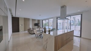 Eine moderne Küche mit Kochinsel, ein Essbereich mit Sofa und große Fenster mit Blick ins Freie.