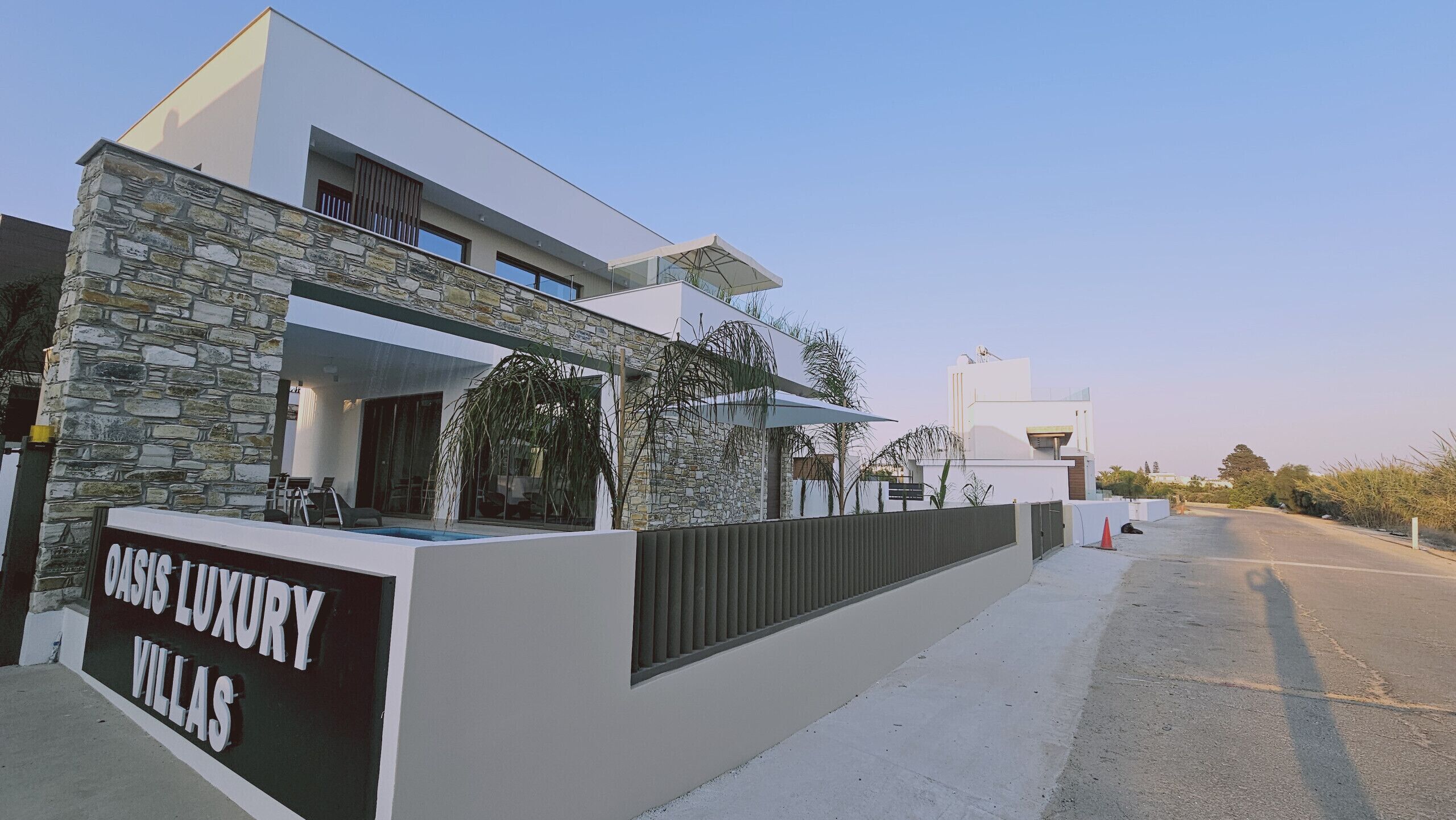 Uma villa moderna com fachada de pedra, piscina e uma placa com a inscrição "Oasis Luxury Villas".