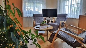 Ein Wohnzimmer mit einer Couch, einem Fernseher und einem Tisch mit einer Pflanze.