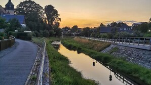 Eine friedliche Flusslandschaft mit einem Kirchturm, einem gepflasterten Weg und Wohngebäuden.