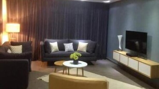 A modern living room with a dark-colored sofa, a small round coffee table with a plant, and a flat-screen TV on a wooden cabinet. - Luxueux Appartement S+3 Avec Jacuzzi - Confort et Élégance (nabeul)