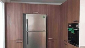 A kitchen with wooden cabinets, a stainless steel refrigerator, and a black oven. - Luxueux Appartement S+3 Avec Jacuzzi - Confort et Élégance (nabeul)