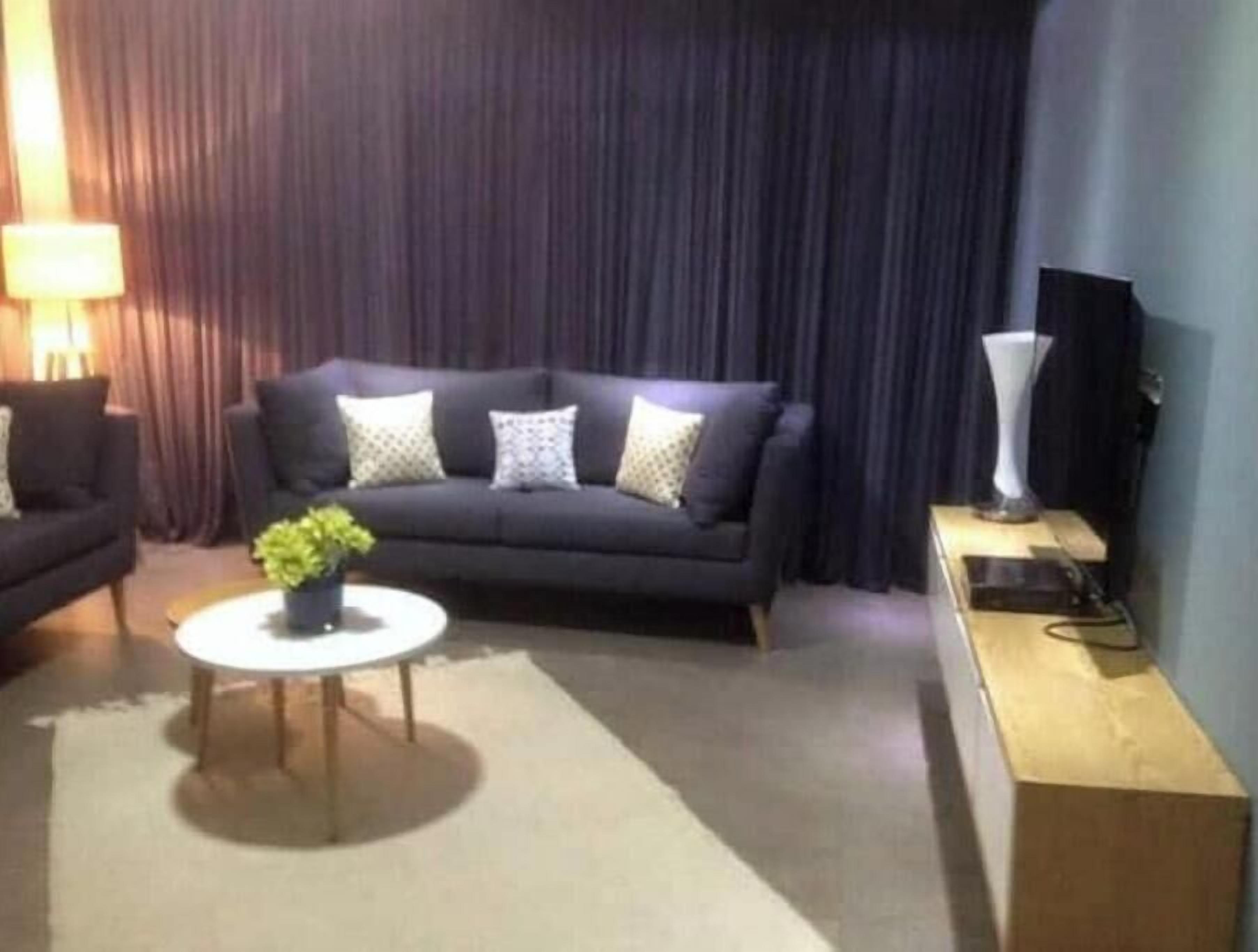 A living room with a dark sofa, a round coffee table with a plant, and a TV on a stand.