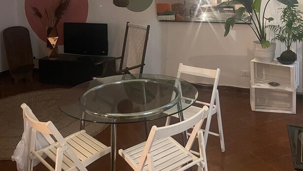 A spacious living area with a glass table surrounded by white chairs, a flat-screen TV, and various plants. - Loft nei caruggi in the heart of superb Genova (Genova)
