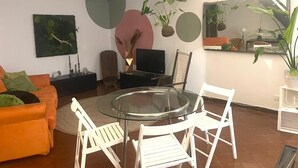 A modern living room with a glass table, white chairs, an orange sofa, and a flat-screen TV. - Loft nei caruggi in the heart of superb Genova (Genova)