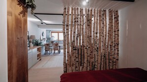 Une chambre avec une armoire en bois, une couverture rouge et un rideau à motifs de bouleau.