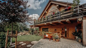 Un chalet en bois doté d’un balcon orné de fleurs, un sentier de pierres menant à un banc en bois et un jardin bien entretenu.
