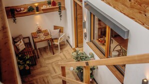 Un escalier en bois mène à un espace repas où se trouvent une table en bois, des chaises et une plante suspendue.