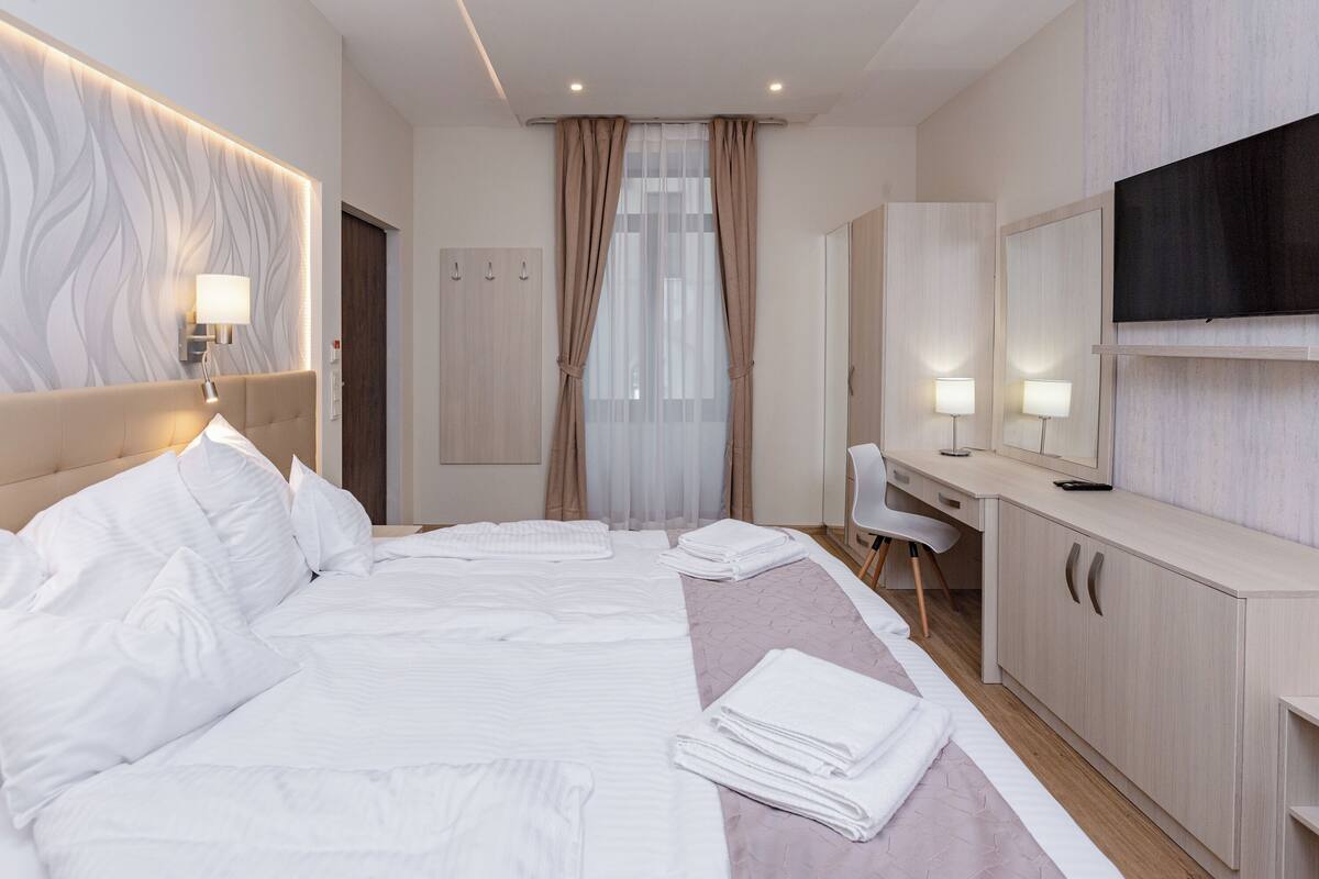 A hotel room with a large bed, a desk, a chair, a TV, and a wardrobe.