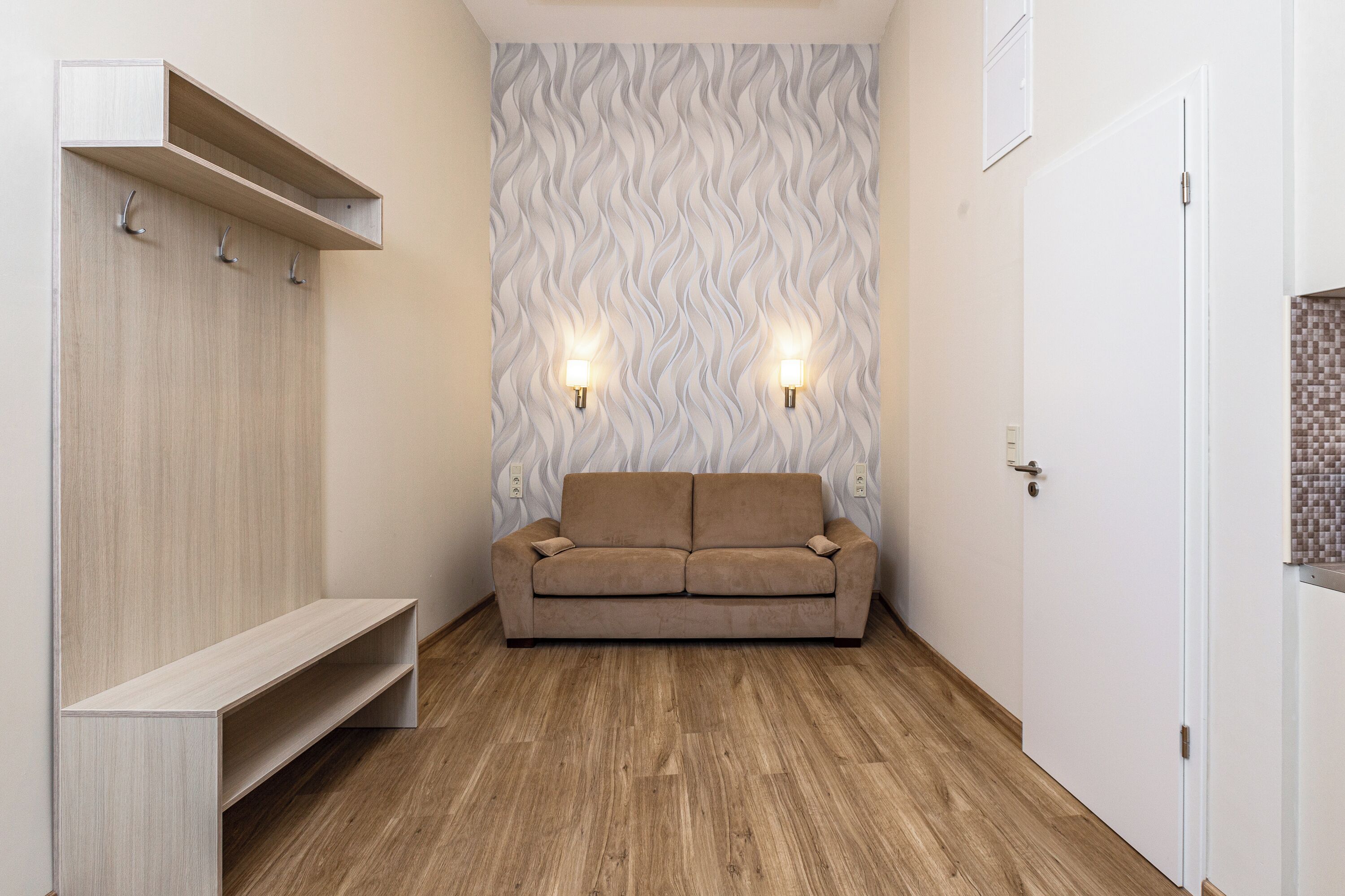 A modern room with a wooden floor, a beige sofa, a built-in bench, and a patterned wall.