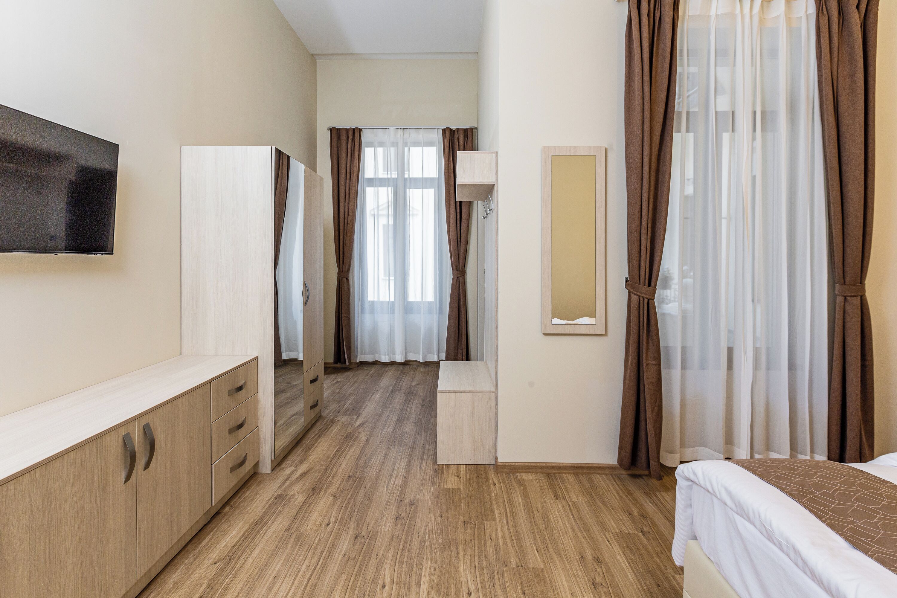 Een hotelkamer met een bed, een televisie, een kledingkast, een spiegel en een badkamer met douche.