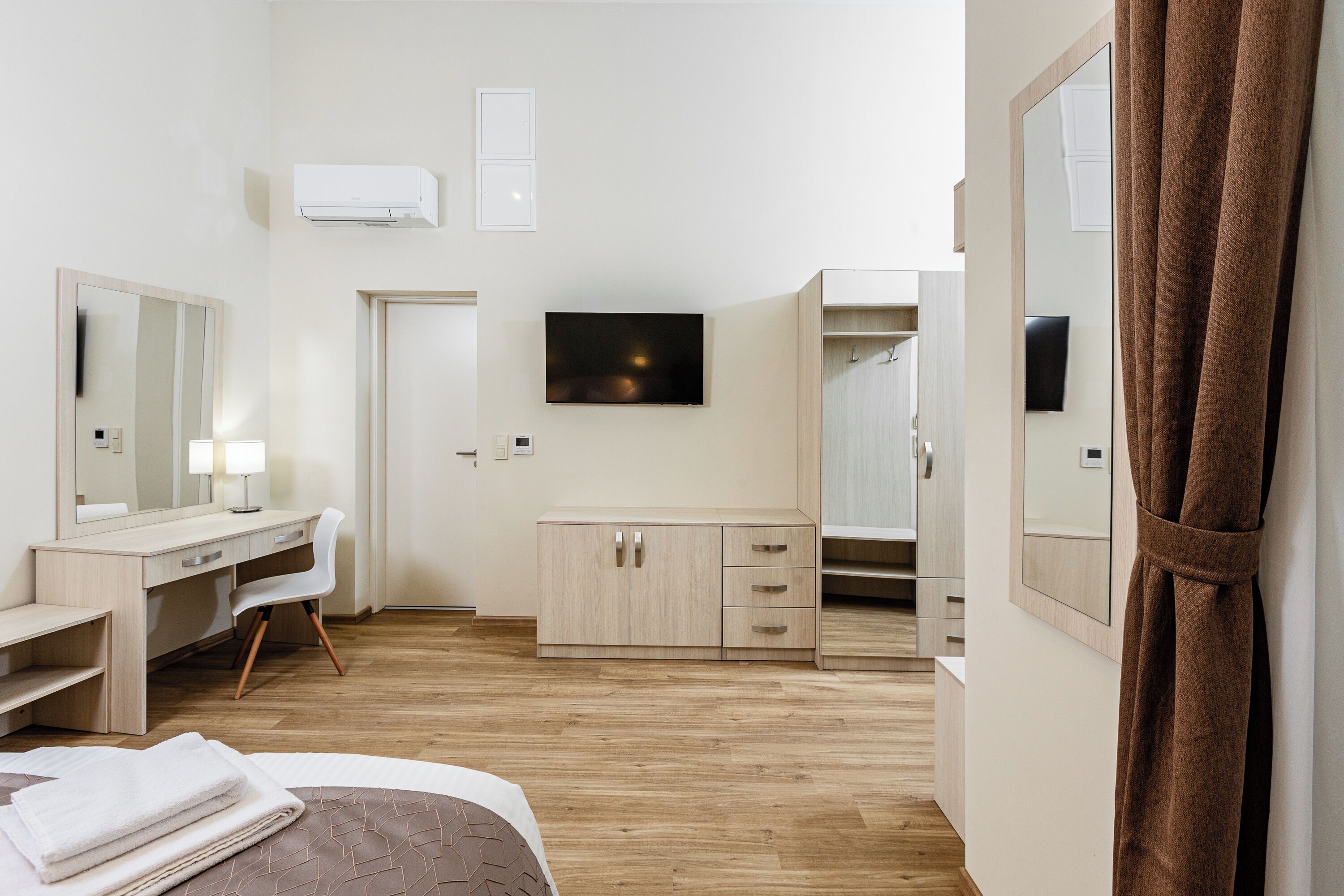 Una habitación de hotel moderna con cama, escritorio, silla, armario y televisor.