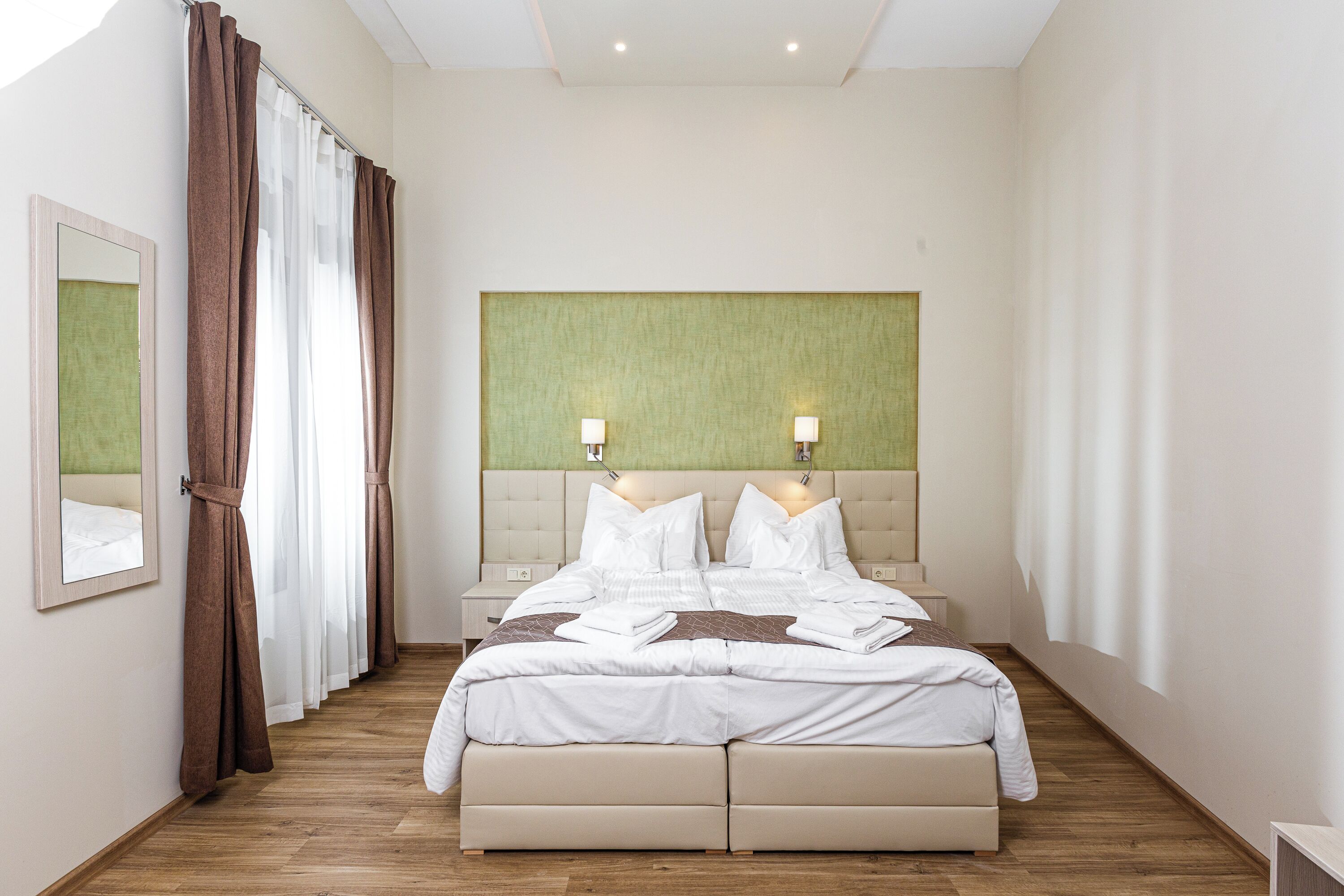 A hotel room with a large bed, two bedside lamps, a headboard, and a mirror on the wall.