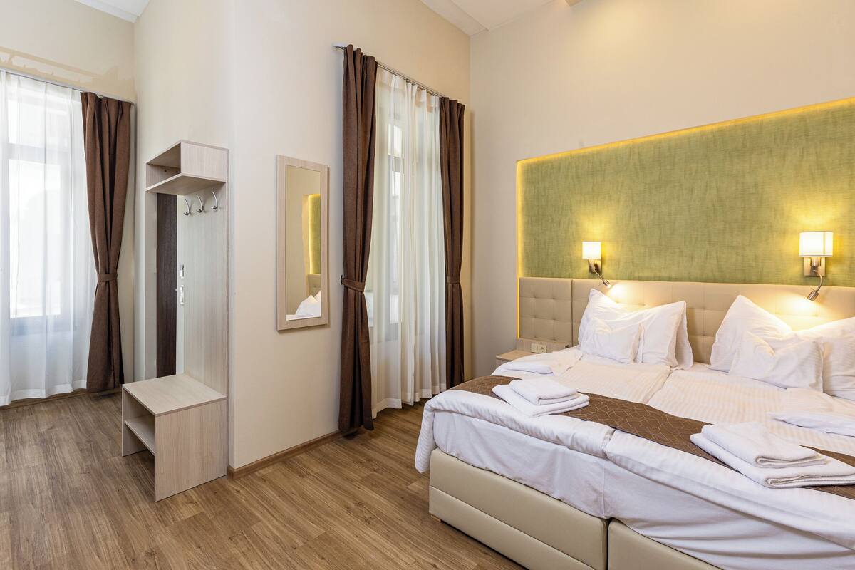 A hotel room with a large bed, a bedside table, a mirror, and a headboard with wall-mounted lights.
