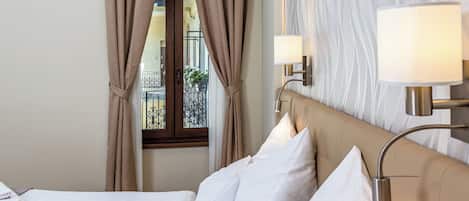 Habitación de hotel con cama, cortinas, ventana con vista a un balcón y lámparas fijadas en la pared.