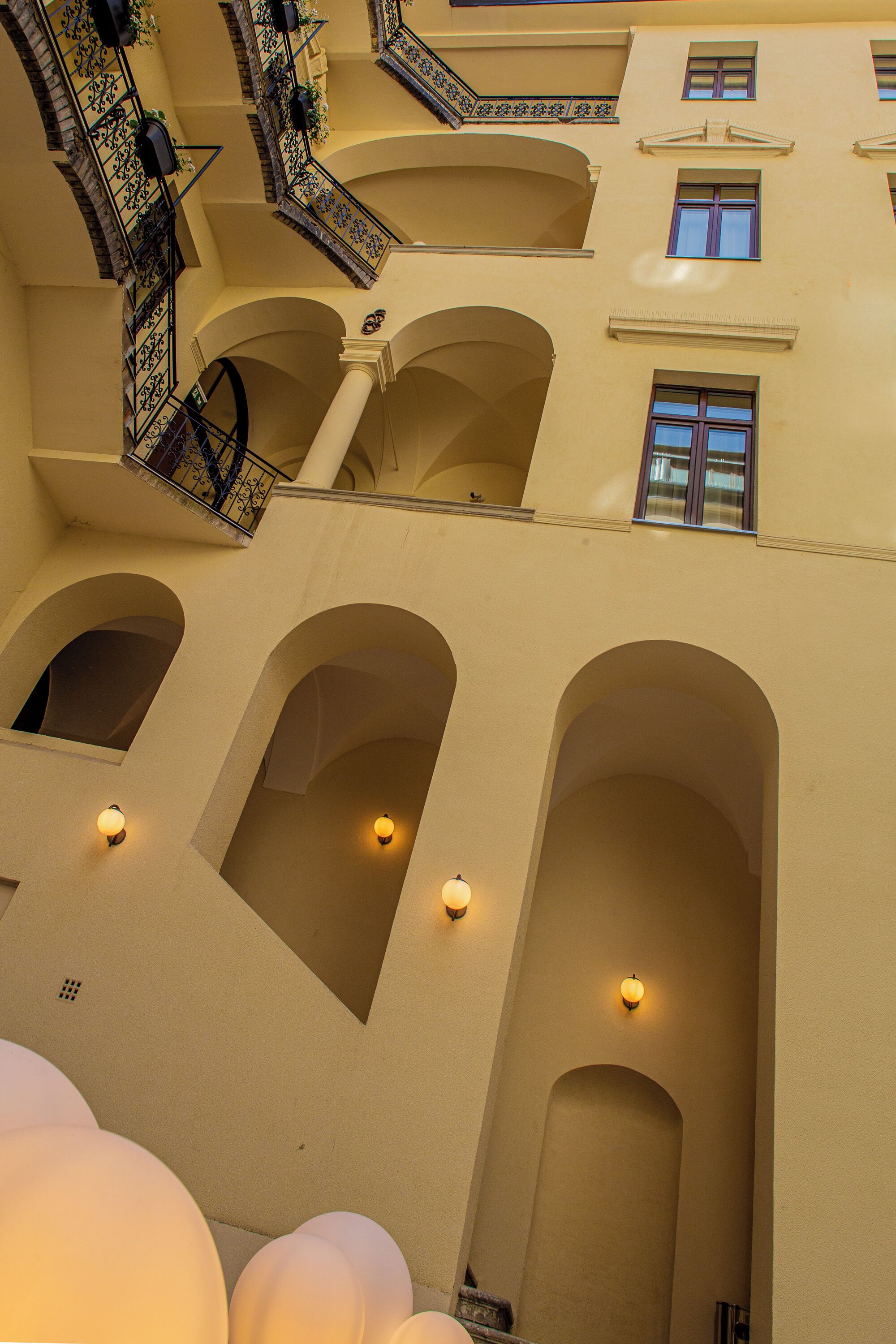Un intérieur à plusieurs niveaux, agrémenté d’alcôves et de balcons en arc de cercle, et caractérisé par un style architectural homogène, avec des murs de couleur claire et des balustrades décoratives.