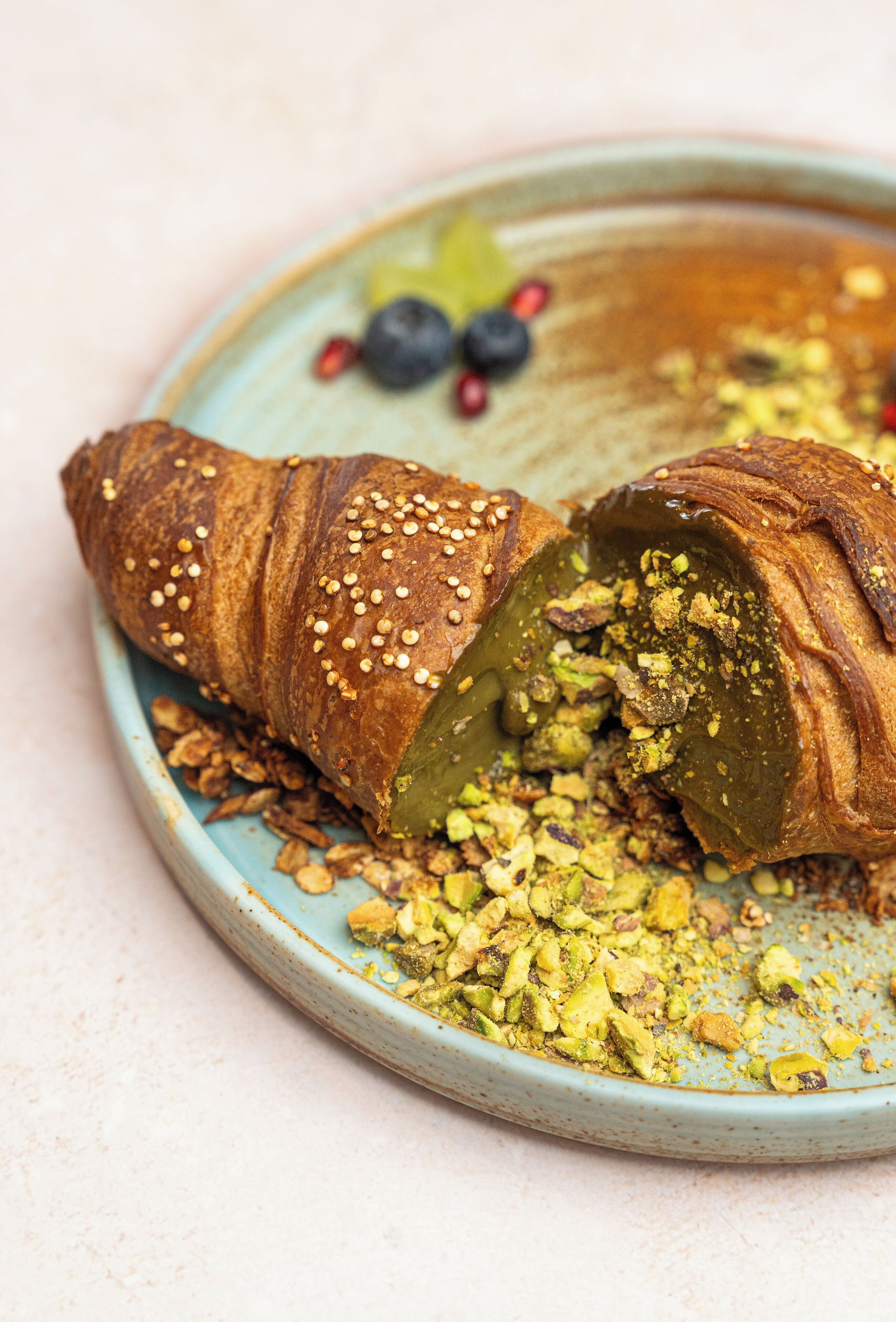 Croissant farcit, daurat amb trossos de fruits secs, sobre un plat de ceràmica amb engrudelades.
