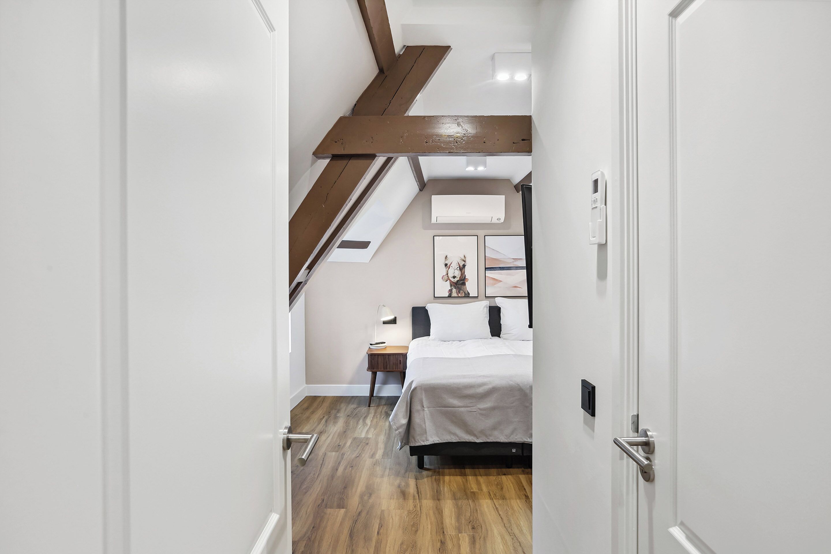 A bedroom with a wooden ceiling, a bed, a nightstand, and a wall-mounted air conditioner.