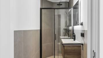 A modern bathroom with a glass shower enclosure, a white sink, and a toilet.