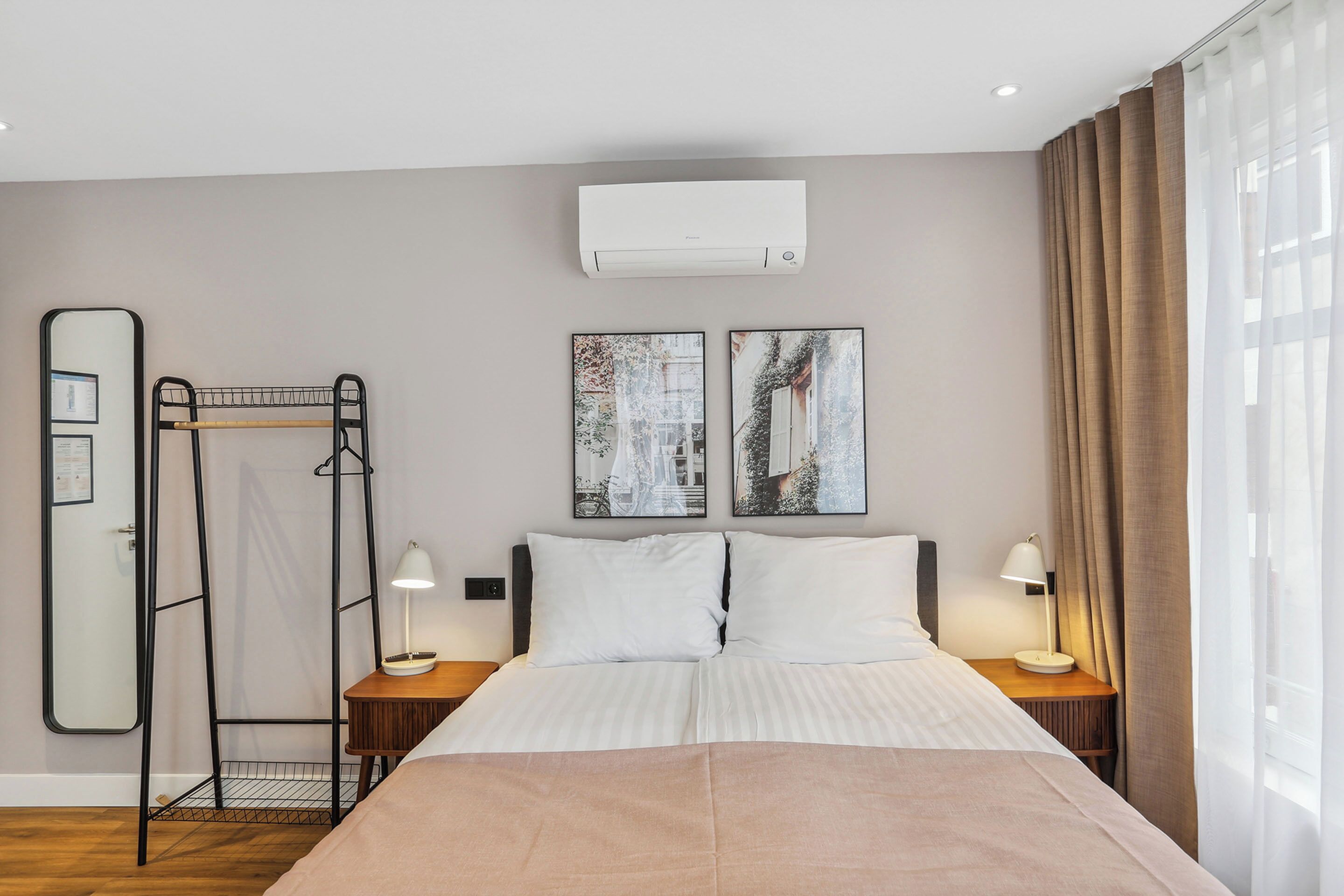 Ein Hotelzimmer mit einem großen Bett, zwei Nachttischen mit Lampen, einer Wandklimaanlage und zwei gerahmten Bildern über dem Bett.