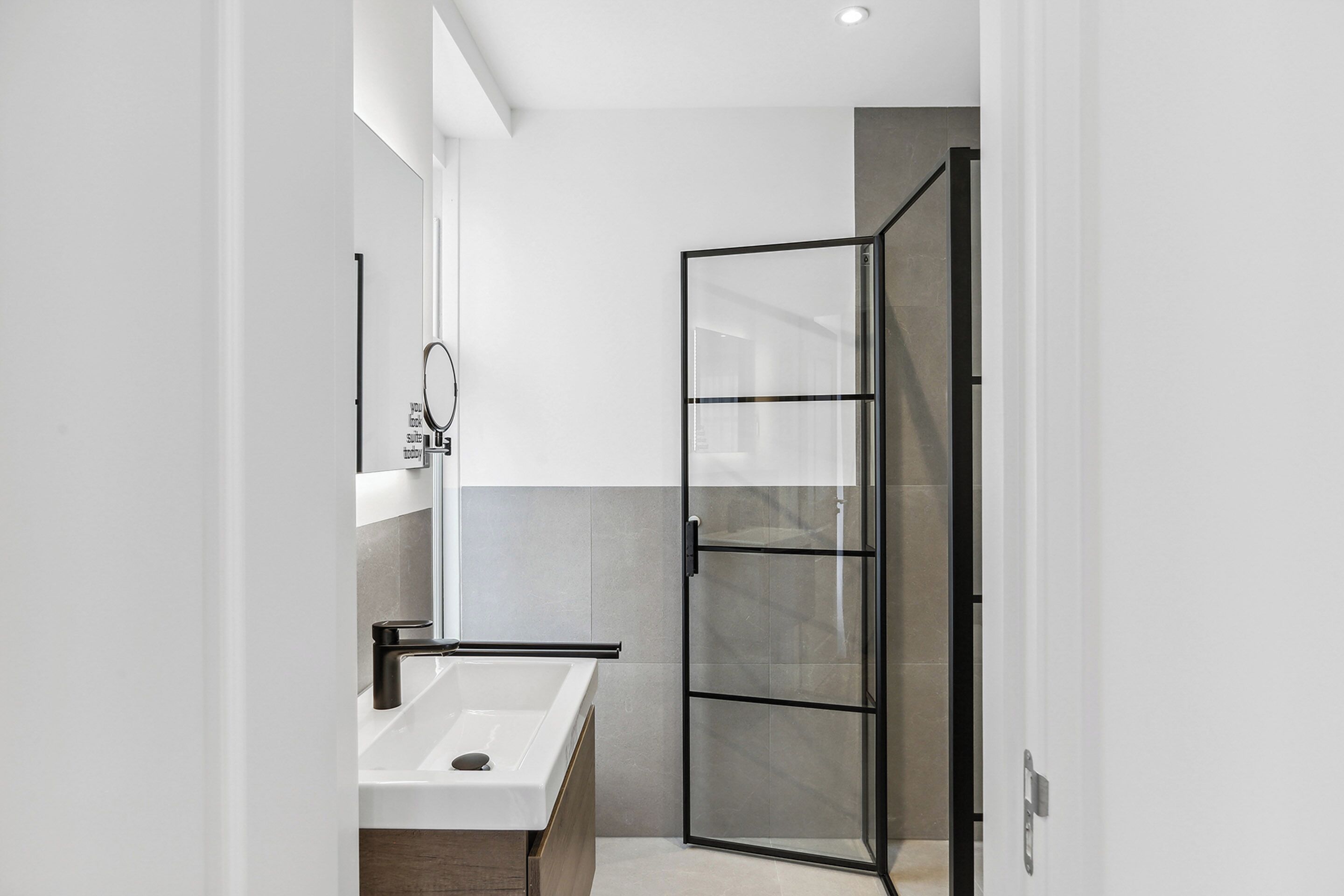 Een moderne badkamer met een douchecabine van glas, een witte wastafel en een spiegel.