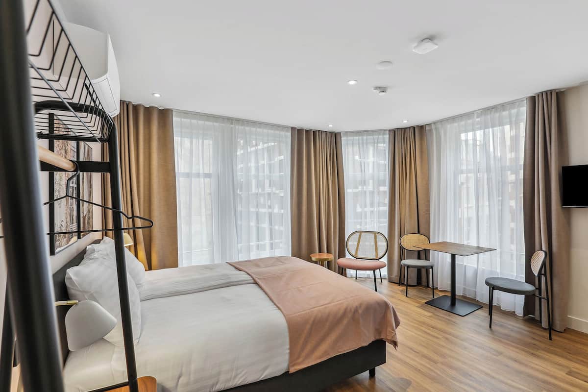 A modern hotel room with a large bed, a desk, two chairs, and a TV.
