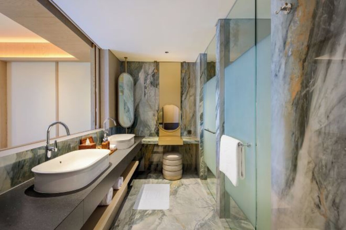 A modern bathroom with a large oval sink, two mirrors, a marble vanity, and a glass shower enclosure.