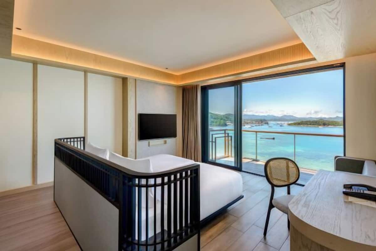 Ein modernes Hotelzimmer mit Balkon, einem Bett, einem Schreibtisch und einem Fernseher.