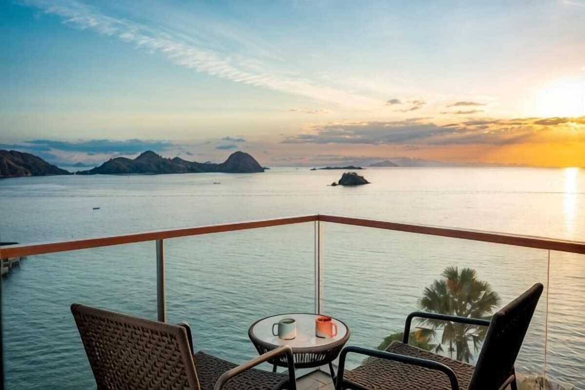 A balcony with a table and chairs overlooking a body of water with distant islands.