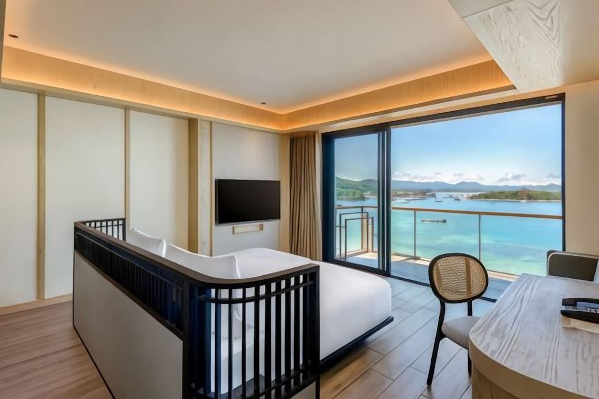 Ett modernt hotellrum med balkong, en platt-TV, en soffa, ett matbord och utsikt över havet.