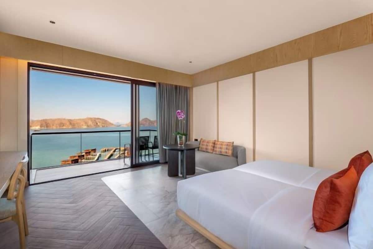 Ein modernes Hotelzimmer mit einem großen Bett, einer Sitzecke mit Blick und einem Balkon mit Meerblick.