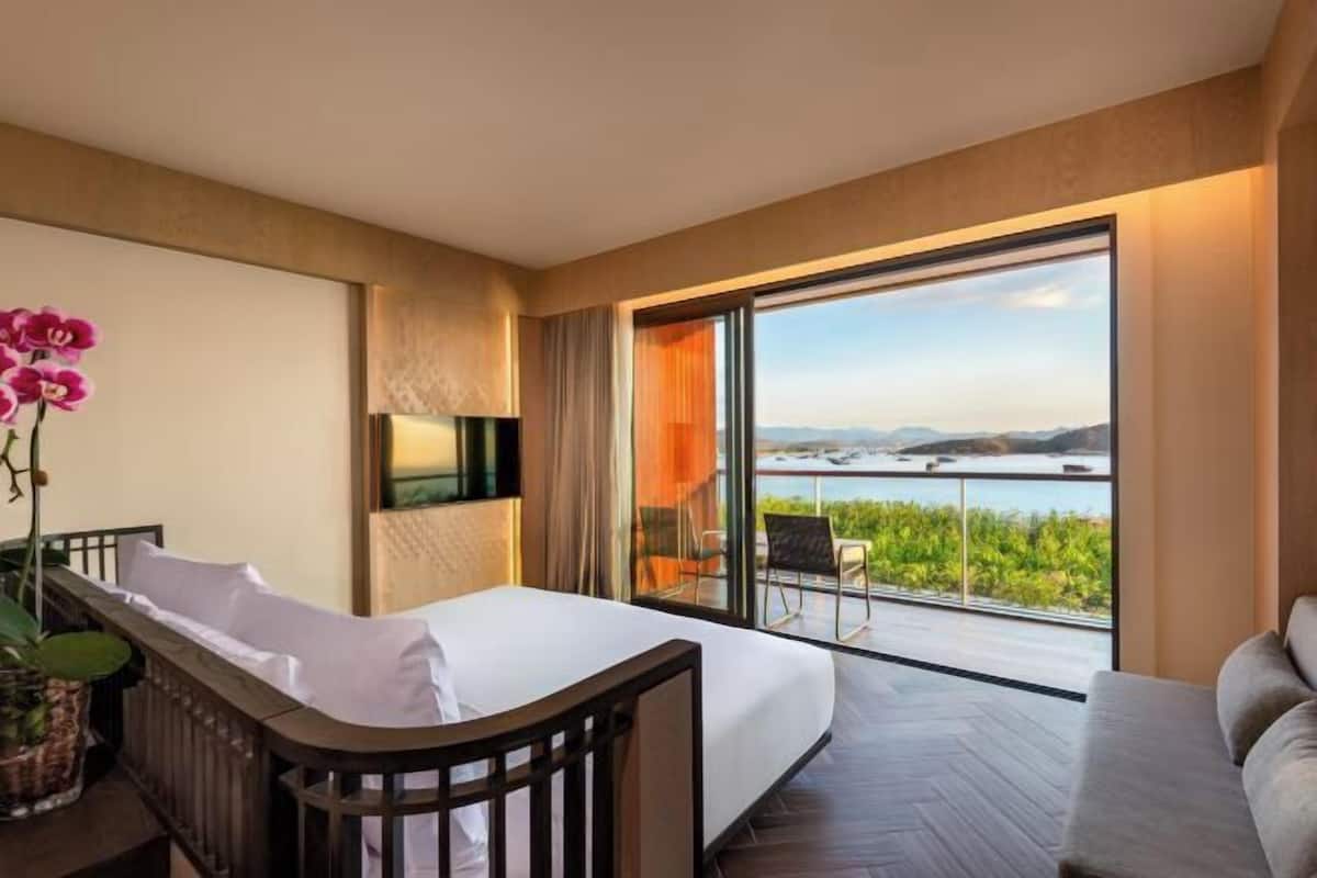 Ein modernes Hotelzimmer mit einem großen Bett, einem Fernseher, einem Balkon mit Meerblick und einer Sitzecke.