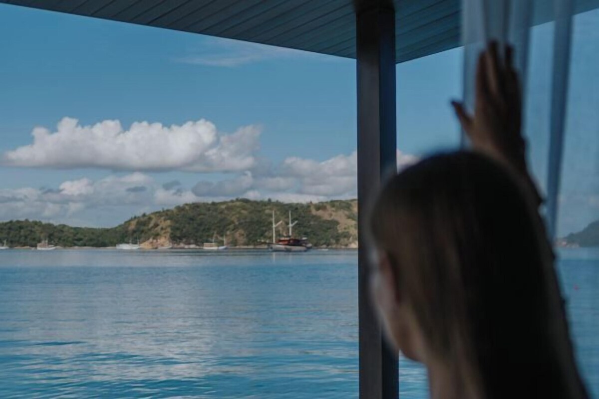 A view from a window overlooking a body of water with a distant landmass and a sailboat.
