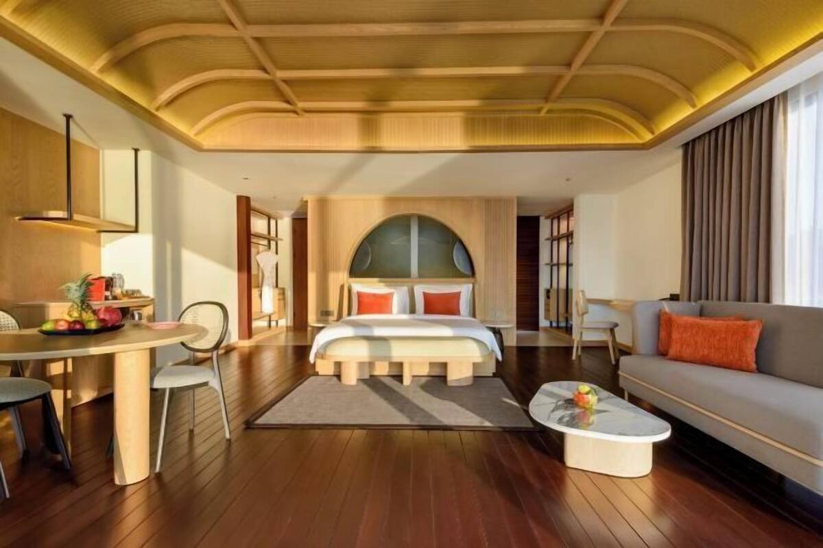 Ein modernes Hotelzimmer mit Holzbalkendecke, einem großen Bett, einer Couch, einem Esstisch und einem kleinen Couchtisch.