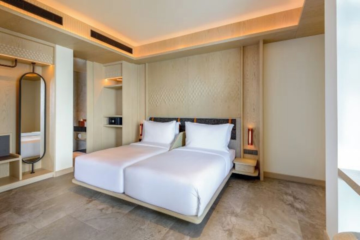 A modern hotel room with a large bed, bedside tables, a mirror, and a wall-mounted light fixture.