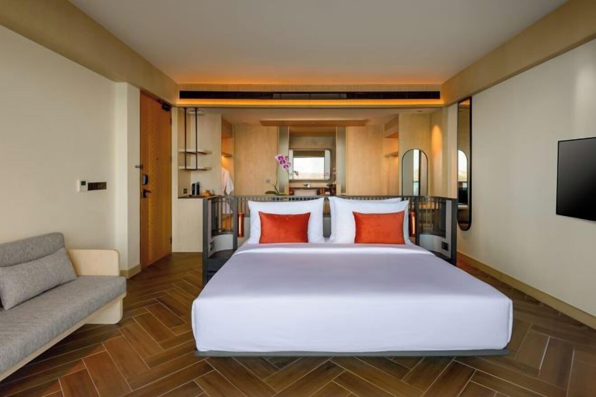 A hotel room with a large bed, a sofa, a TV, and a bathroom visible in the background.