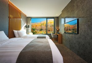 A hotel room with two beds, a desk, and a large window offering a view of autumn foliage. - Jeongseon JS Grand Palace Hotel (Jeongseon)