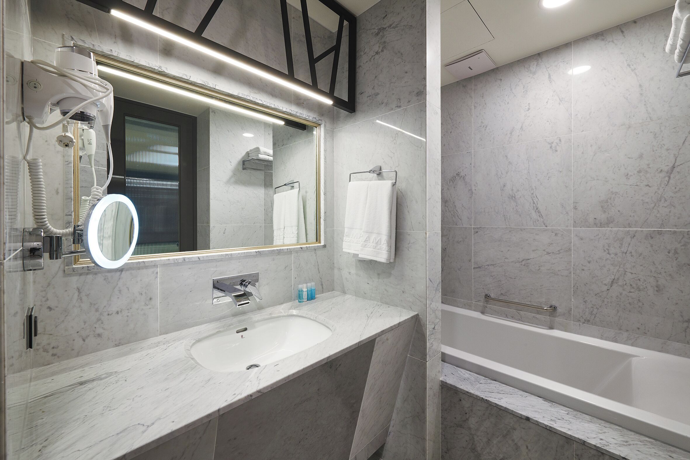 A modern bathroom with a marble sink, a large mirror, and a bathtub.