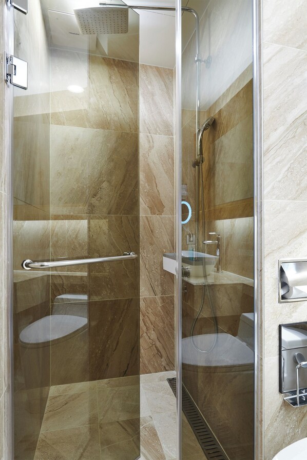 Un baño moderno con ducha envuelta en vidrio, cabezal de ducha manual y un inodoro.