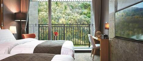 A hotel room with two beds, a desk, and a balcony with a view of trees.