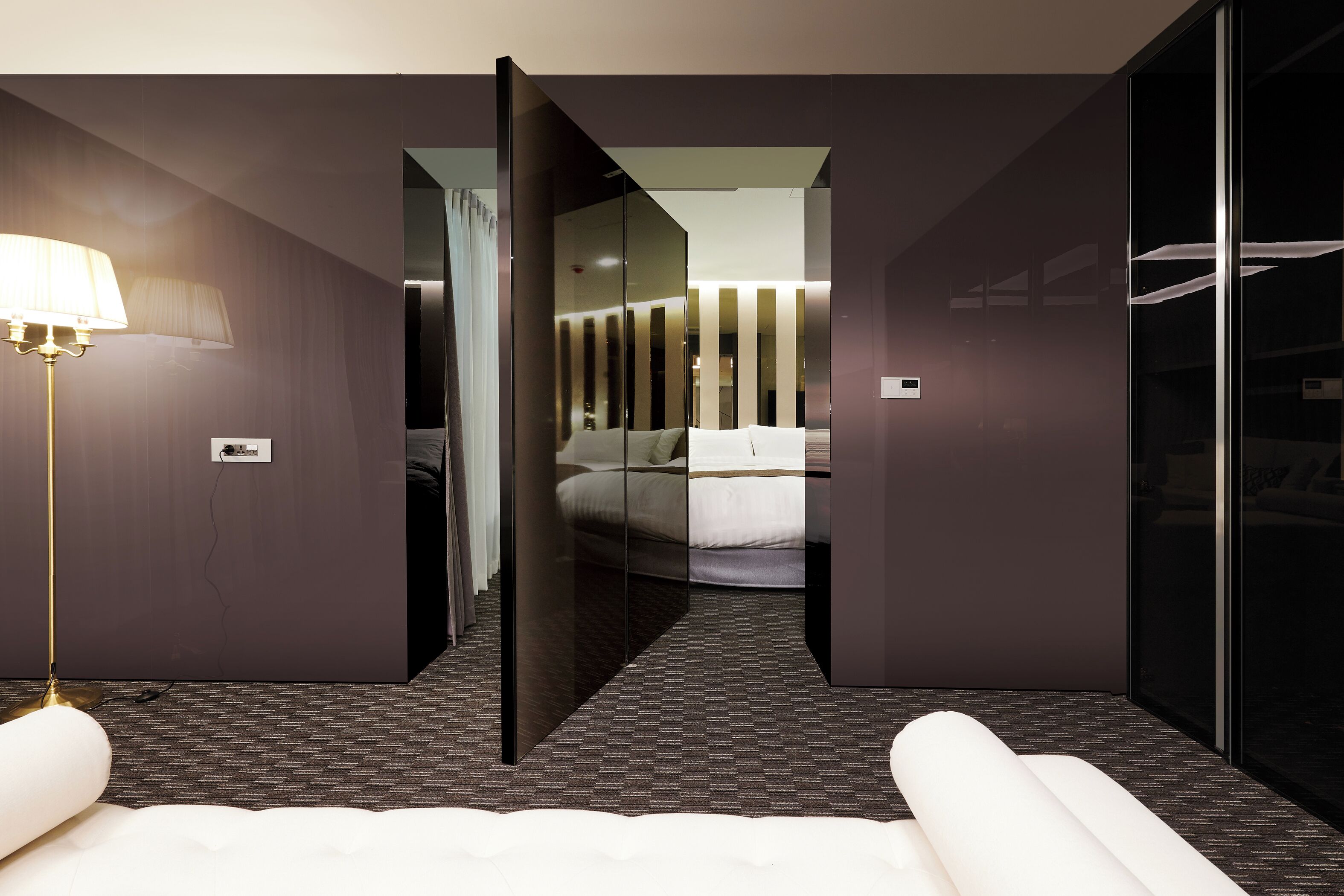 A modern hotel room with a large bed, a bedside lamp, a mirror, and a wardrobe.