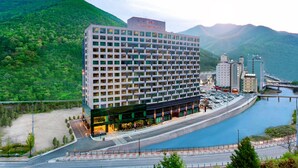 Un hotel modern amb un pati central, envoltat per turons verds i un riu.