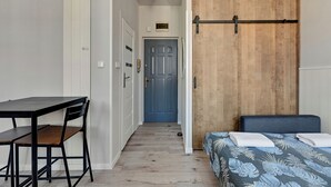 A room with a bed, a desk, and a chair. There is a door in the background.